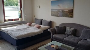 A bedroom with a bed, a sofa, a coffee table, a window with blinds, and a wall-mounted picture. - Cozy vacation apartment quiet in Lindlar-Linde, approx. 30 km from Cologne (Lindlar)