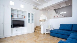Ein Wohnzimmer mit Fernseher, weißen Schränken, einem blauen Sofa und einer Treppe.