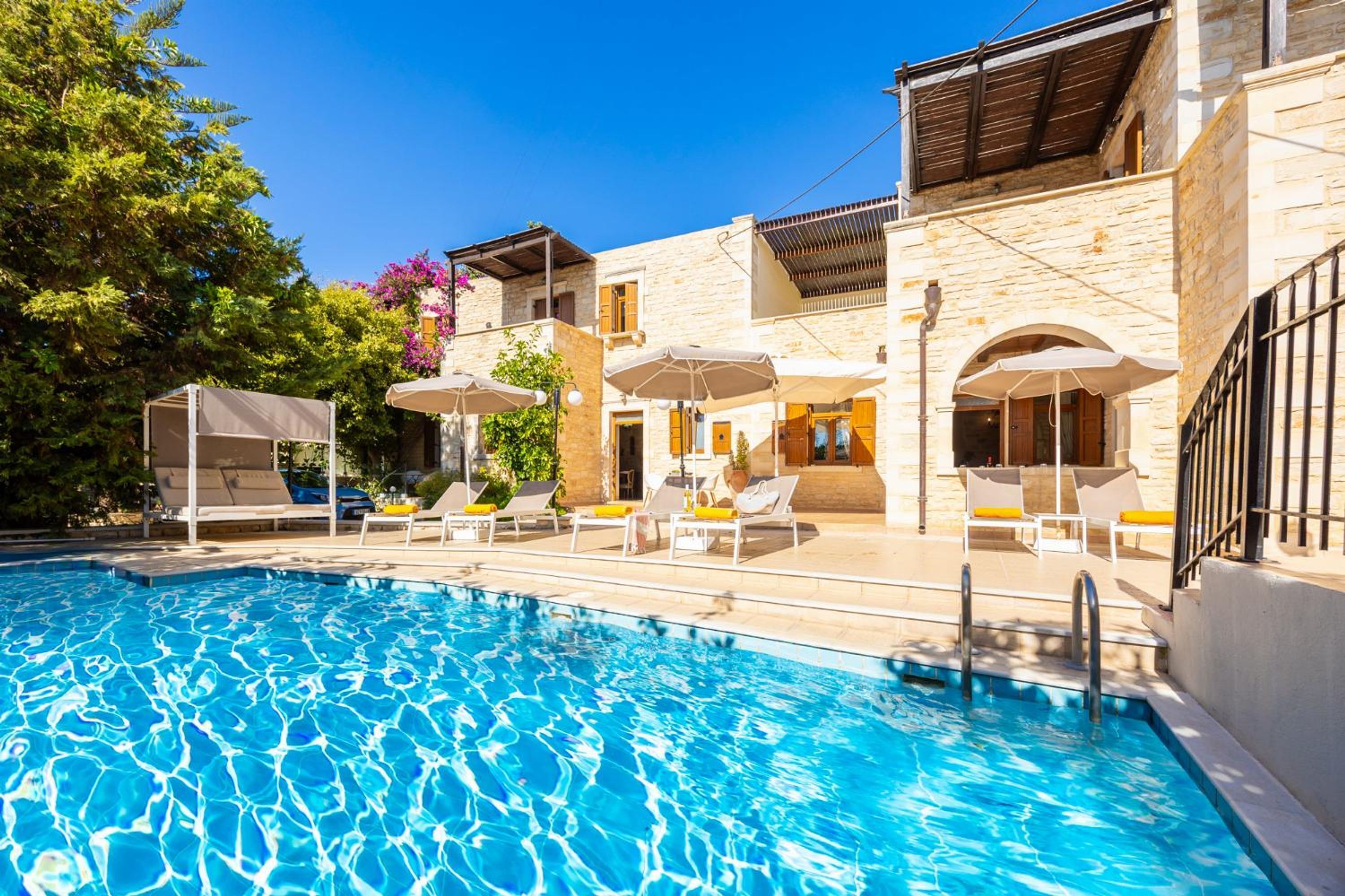 Une piscine entourée de bâtiments en pierre dotés de balcons, avec des chaises longues et des parasols à proximité.
