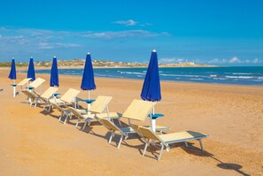 A beach with rows of sun loungers and blue umbrellas, a clear sky, and the ocean in the background. - Villa Nina in Scicli (Scicli)