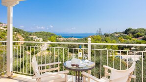 A balcony with white railings, two white chairs, a small round table with a bottle of wine, a glass, and a book. - Villa Magda Dione in Gaios (Paxos)