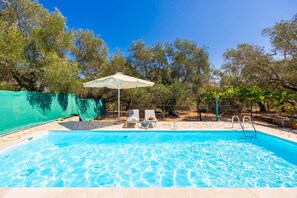 A swimming pool with two lounge chairs and a table under a canopy, surrounded by trees. - Villa Old Vineyard in Paxi (Paxos)