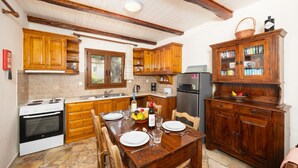 A kitchen with wooden cabinets, a dining table set for four, and a refrigerator. - Villa Old Vineyard in Paxi (Paxos)