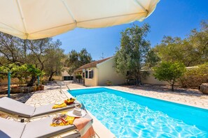 A swimming pool with lounge chairs and umbrellas, surrounded by trees and a building. - Villa Old Vineyard in Paxi (Paxos)