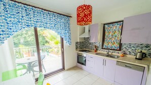 A modern kitchen with a gas stove, oven, and dishwasher, a dining area with a table and chairs, and a balcony with a view of greenery. - Villa Garden Island in Dalyan (Ortaca)