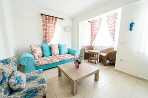 A living room with a sofa, a coffee table, a wicker chair, and a small table with a chair. - Villa Garden Island in Dalyan (Ortaca)