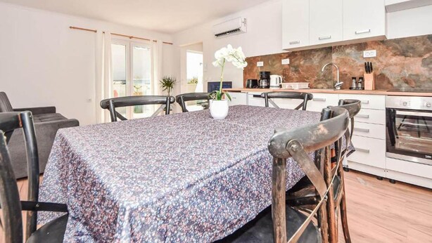 A modern kitchen with white cabinets, a granite countertop, and a dining area with a table set for four. - Villa Lara in Sveti Filip i Jakov (Sveti Filip i Jakov)