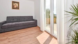A modern living room with a grey sofa, wooden flooring, a large sliding glass door leading to an outdoor area, and a framed picture on the wall. - Villa Lara in Sveti Filip i Jakov (Sveti Filip i Jakov)