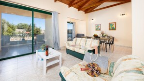 A spacious living area with a green sofa, a white coffee table, and a dining table with chairs. A large sliding glass door leads to an outdoor patio. - Villa Iris in Kefalas (Apokoronas)
