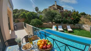 A poolside view with a table set with fruits and olives, lounge chairs, and a stone wall. - Villa Iris in Kefalas (Apokoronas)