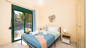 A bedroom with a bed, a nightstand, a wardrobe, a sliding glass door, and a view of the outside. - Villa Iris in Kefalas (Apokoronas)