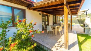 Une terrasse couverte avec une table et des chaises, un barbecue et une vue sur un paysage montagneux.