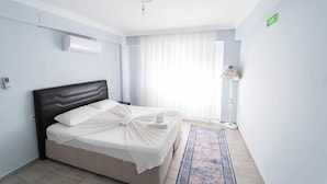 Une chambre d’hôtel avec un lit, une table de chevet, une lampe sur pied et une fenêtre avec des rideaux.