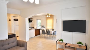 A modern living room with a sofa, a coffee table, and a TV. There is a dining area with a table and chairs, and a kitchen in the background. - Villa Rosetta in Oludeniz (Fethiye)