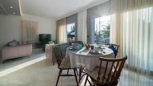 A modern living room with a dining area, large windows, and a flat-screen TV. - Villa Riva in Oludeniz (Fethiye)