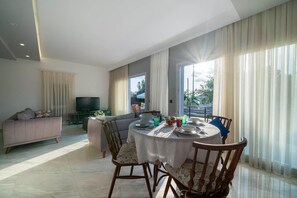 A modern living room with a dining area, large windows, and a flat-screen TV. - Villa Riva in Oludeniz (Fethiye)