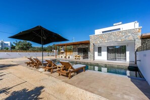 A modern house with a swimming pool, outdoor seating, and a stone facade. - Villa Serenita in Afandou (Rhodes)