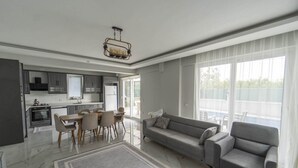 A modern living room with a grey sofa, a dining area with a table and chairs, and a kitchen with grey cabinets and a built-in oven. - Villa Maya in Ortaca (Ortaca)