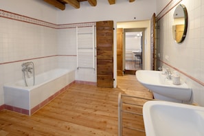 A bathroom with a wooden floor, a bathtub, a sink, and a mirror.