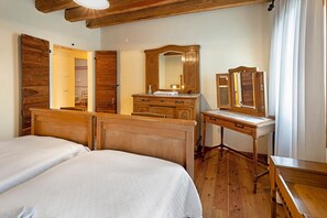 A bedroom with two beds, wooden furniture, a dresser, a mirror, and a wooden ceiling.