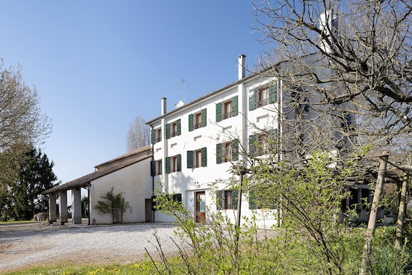 A multi-story building with a white facade, green shutters, and a gravel driveway.