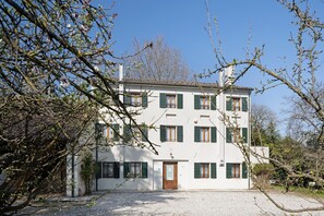 Un edificio de dos pisos con fachada blanca, contraventanas verdes y entrada de grava.