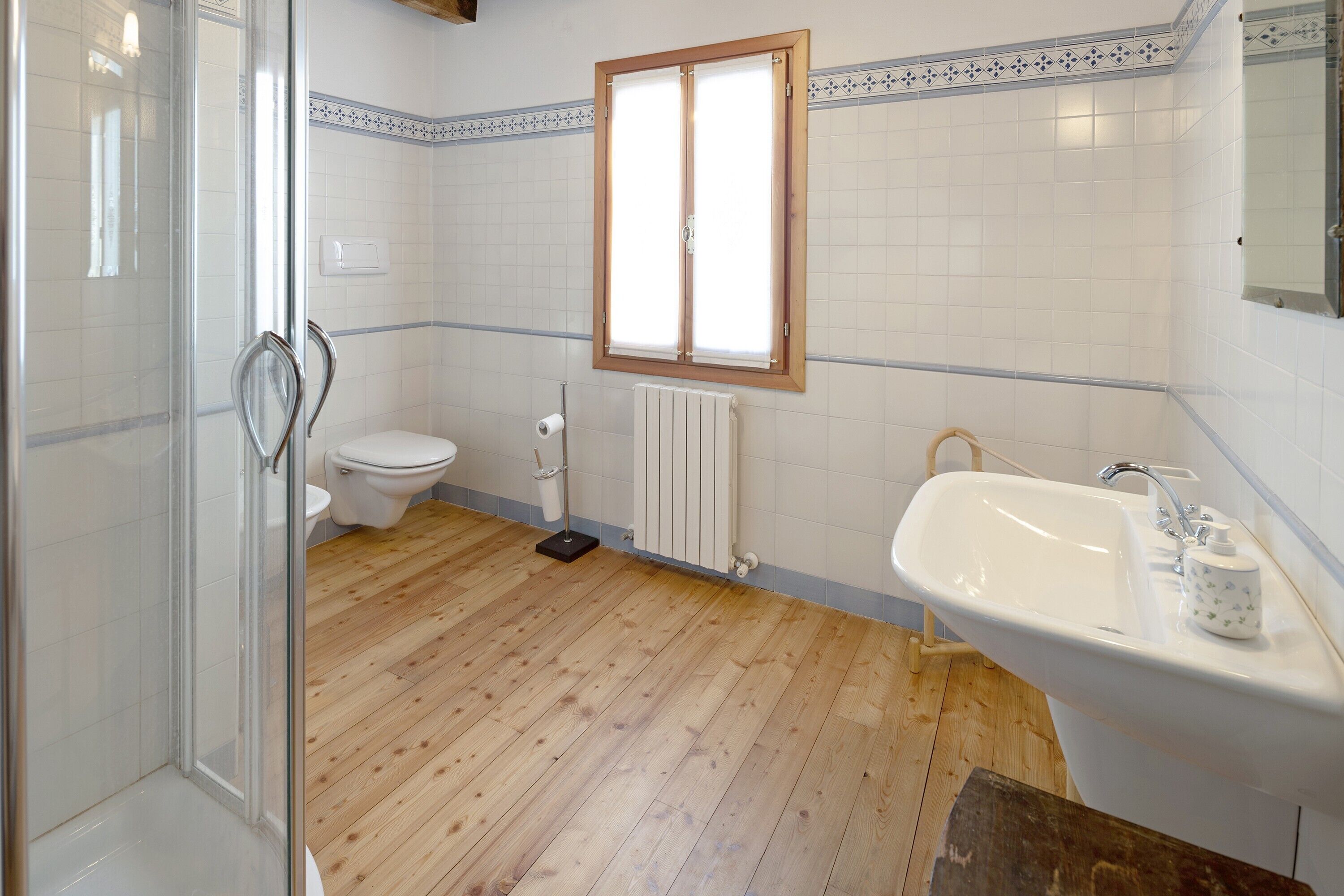 A bathroom with a shower, toilet, radiator, and sink.