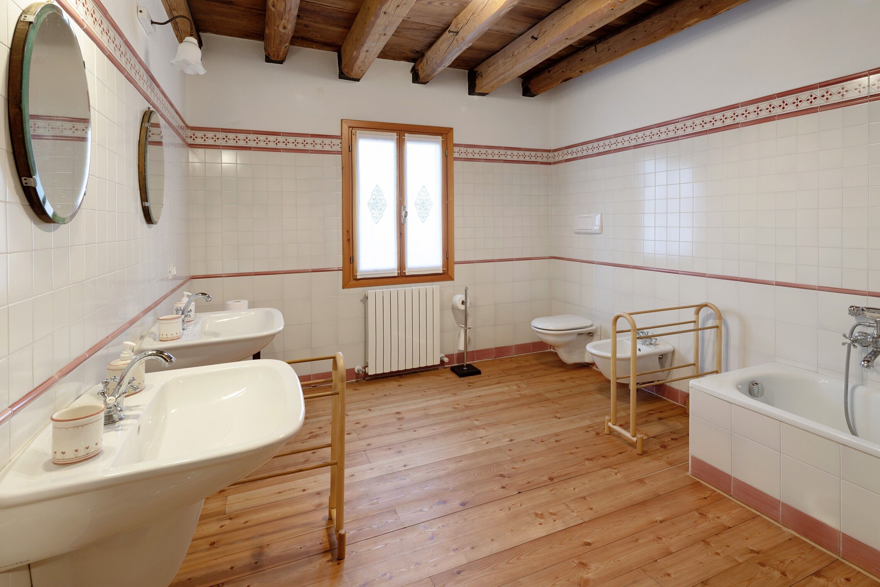 Ein Badezimmer mit Holzboden, zwei Waschbecken, einer Toilette, einer Badewanne und einem Fenster.