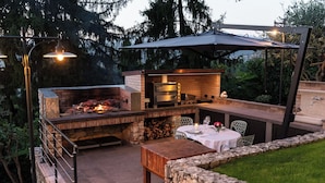 Un patio exterior con chimenea de ladrillo, una parrilla y una mesa lista para comer.