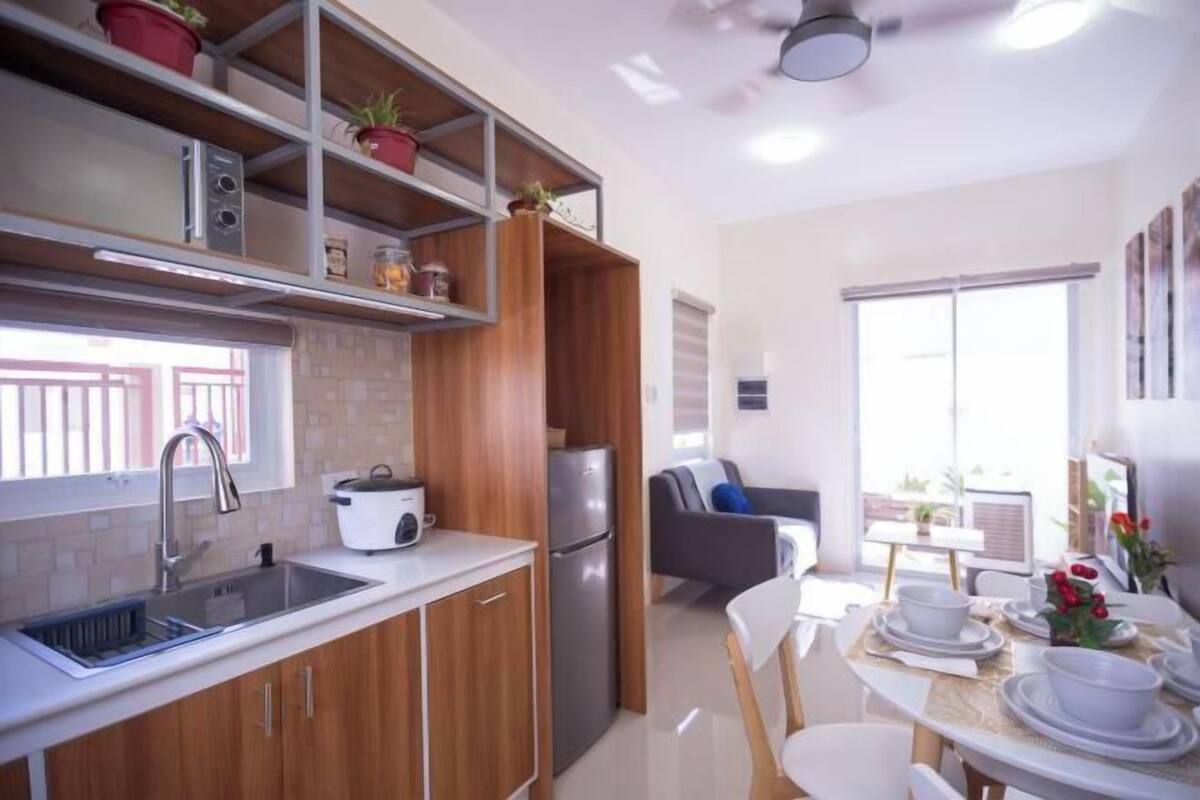 Una cocina moderna con armarios de madera, un horno empotrado y un comedor con sillas blancas y una mesa preparada para dos.