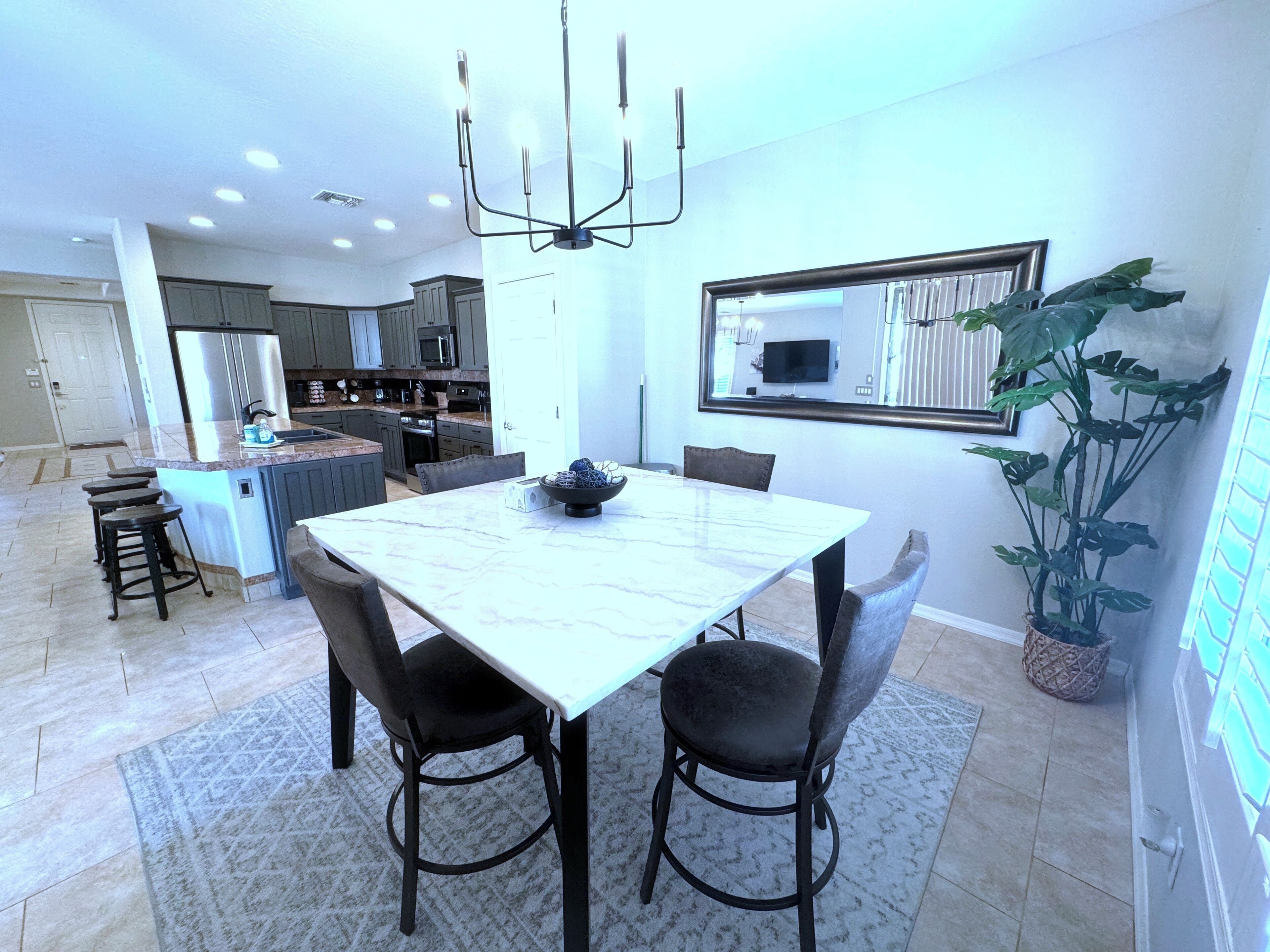 A modern kitchen with dark cabinets, a central island, and a dining area with a marble table and four chairs.