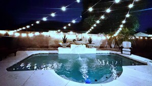 Ein Swimmingpool mit Steinkante, umgeben von einer niedrigen Mauer und Lichterketten.