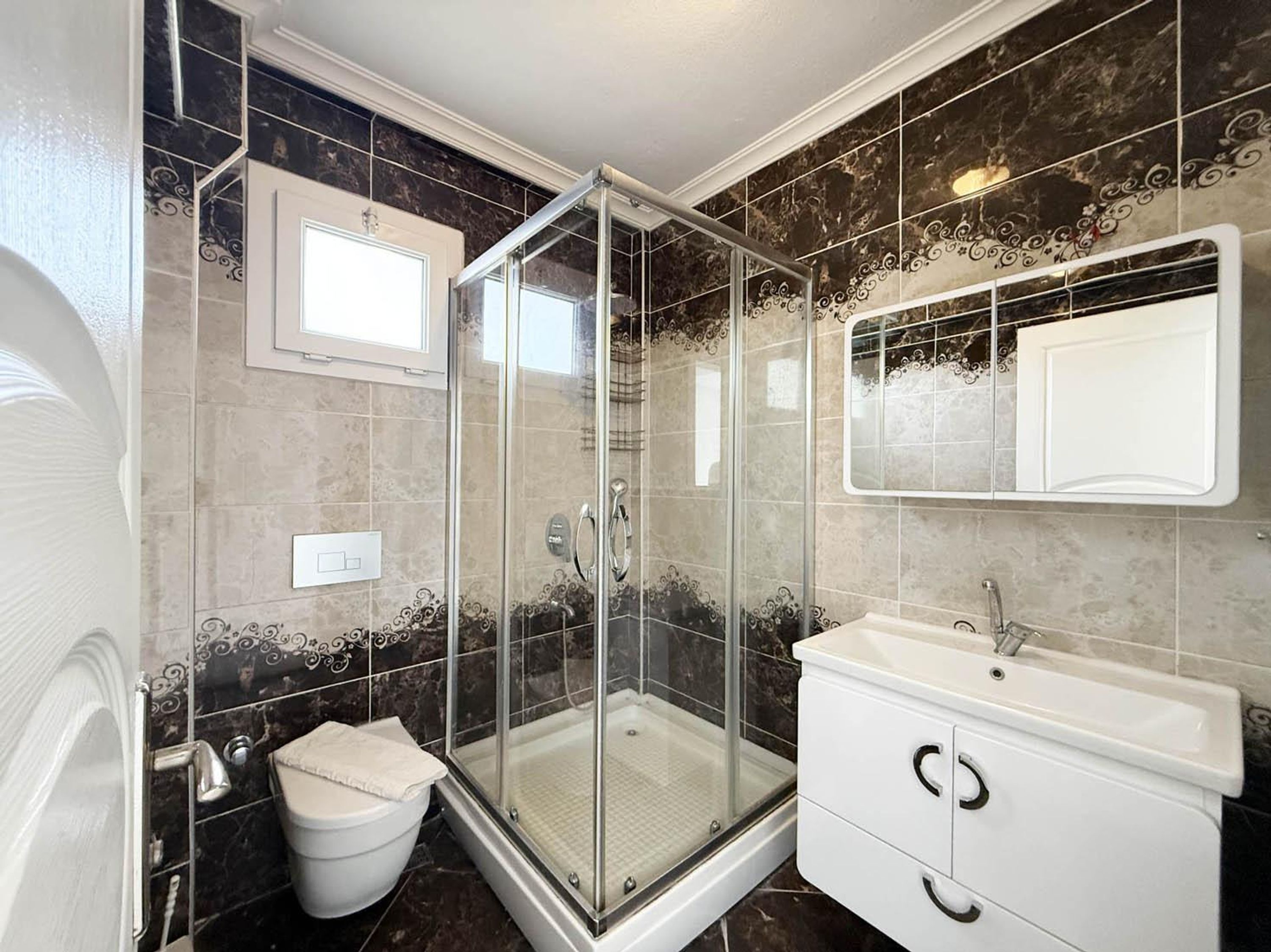 Ein Badezimmer mit Duschkabine aus Glas, Waschbecken in Weiß und Toilette.