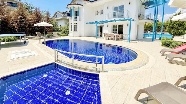 A swimming pool area with a white building, lounge chairs, and a covered seating area.