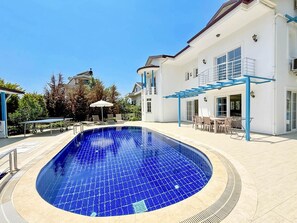 A swimming pool with a blue tiled floor, surrounded by a white building with a balcony and outdoor seating area. - Villa Fergana in Oludeniz (Fethiye)
