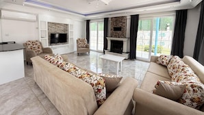 A spacious living room with a fireplace, large windows, and a flat-screen TV.