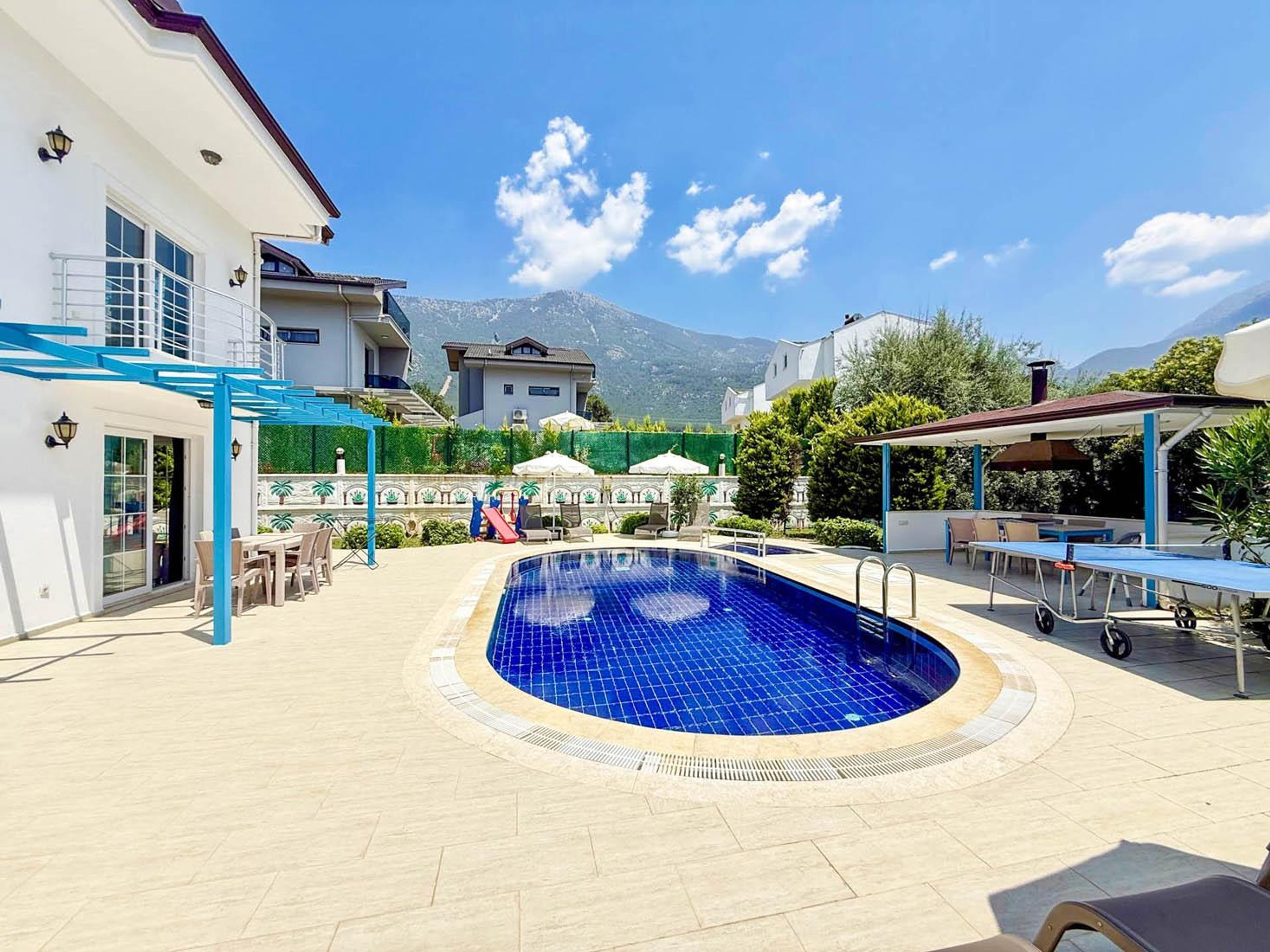 A swimming pool with a blue tiled interior, surrounded by a patio area with outdoor furniture and a covered seating area.