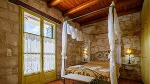 A bedroom with a four-poster bed, stone walls, a wooden ceiling, and a yellow door. - Villa Faidra in Agios Dimitrios (Zakynthos)