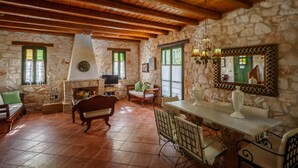 A rustic room with stone walls, wooden beams, a fireplace, a dining table with chairs, and a television. - Villa Faidra in Agios Dimitrios (Zakynthos)