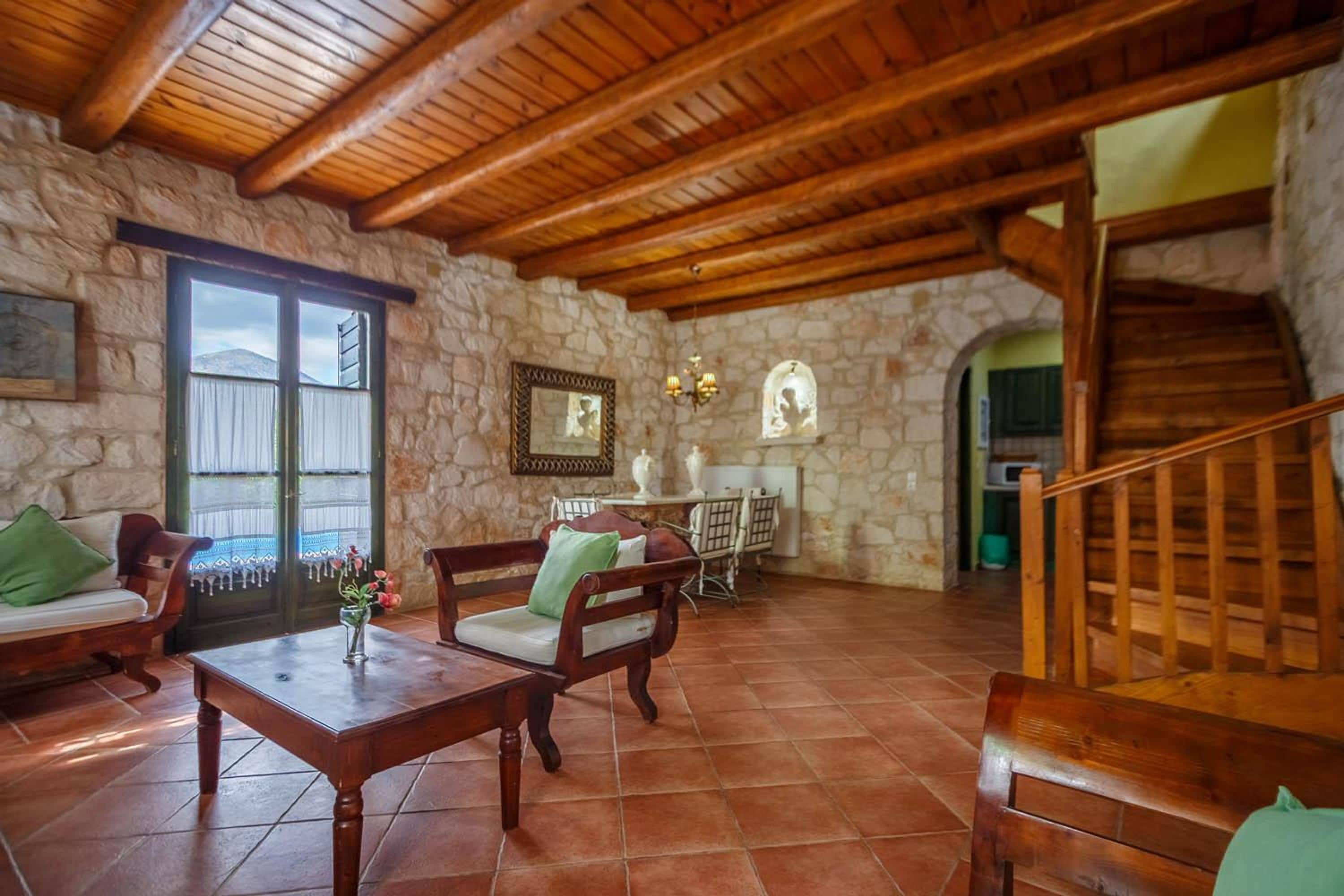 A rustic interior with stone walls, wooden furniture, a staircase, and a view through a window.