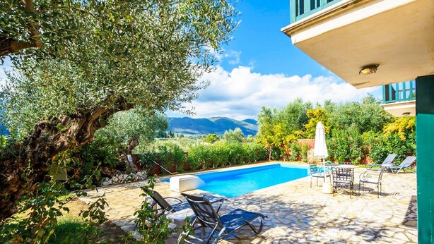 A pool area with stone flooring, lounge chairs, and a view of mountains. - Villa Faidra in Agios Dimitrios (Zakynthos)