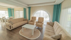 A spacious living room with a beige sofa, two armchairs, a coffee table, and a dining area with a table and chairs. - Villa Everest in Oludeniz (Dalaman)