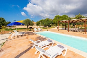 A swimming pool with lounge chairs and umbrellas, surrounded by greenery and a pergola. - Villa Fenice in Scicli (Scicli)