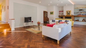 Un salon spacieux avec un canapé blanc, un téléviseur, un meuble en bois et une cheminée.