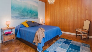 Une chambre à coucher avec un grand lit, des murs en bois, un lustre, une chaise et un tableau représentant une vague.