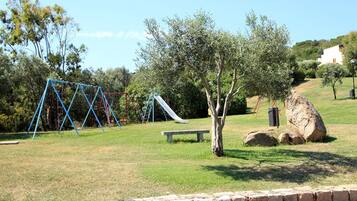 Ein Park mit Schaukeln, einer Rutsche, einer Bank und einem Baum.