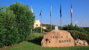 Ein Steinschild mit der Aufschrift "TANCA MANNÄ", umgeben von Grünpflanzen und Flaggen.