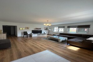 A spacious living room with a large sofa, a coffee table, and a TV. There are framed pictures on the wall and a chandelier. - Elegant 4-Bedroom, 3-Bathroom Apartment in the Heart of Ilidža, Sarajevo (Ilidža)