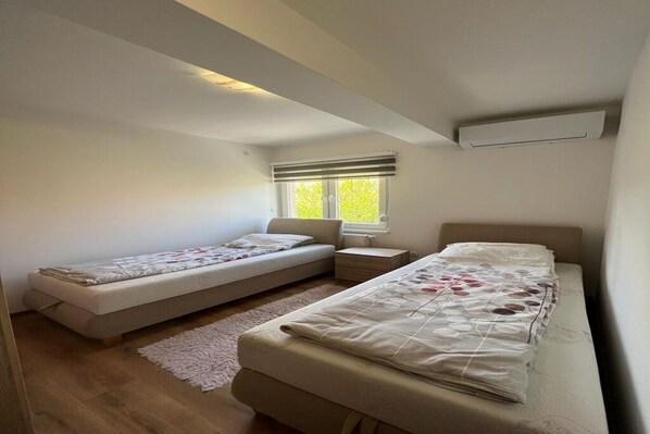 A bedroom with two single beds, a small bedside table, a radiator, and a window with blinds. - Elegant 4-Bedroom, 3-Bathroom Apartment in the Heart of Ilidža, Sarajevo (Ilidža)