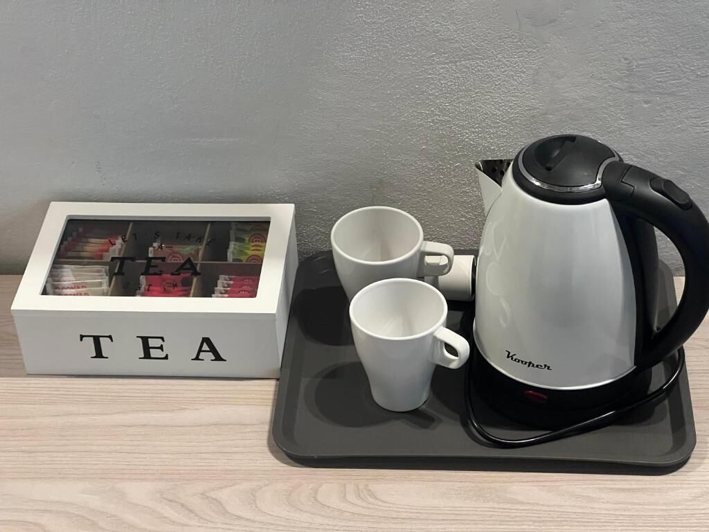 Un plateau à thé avec une théière et deux tasses blanches, le tout posé sur un plateau noir, à côté d’une boîte blanche portant l’inscription « THÉ » et sur laquelle on peut voir une image de sachets de thé à l’intérieur.